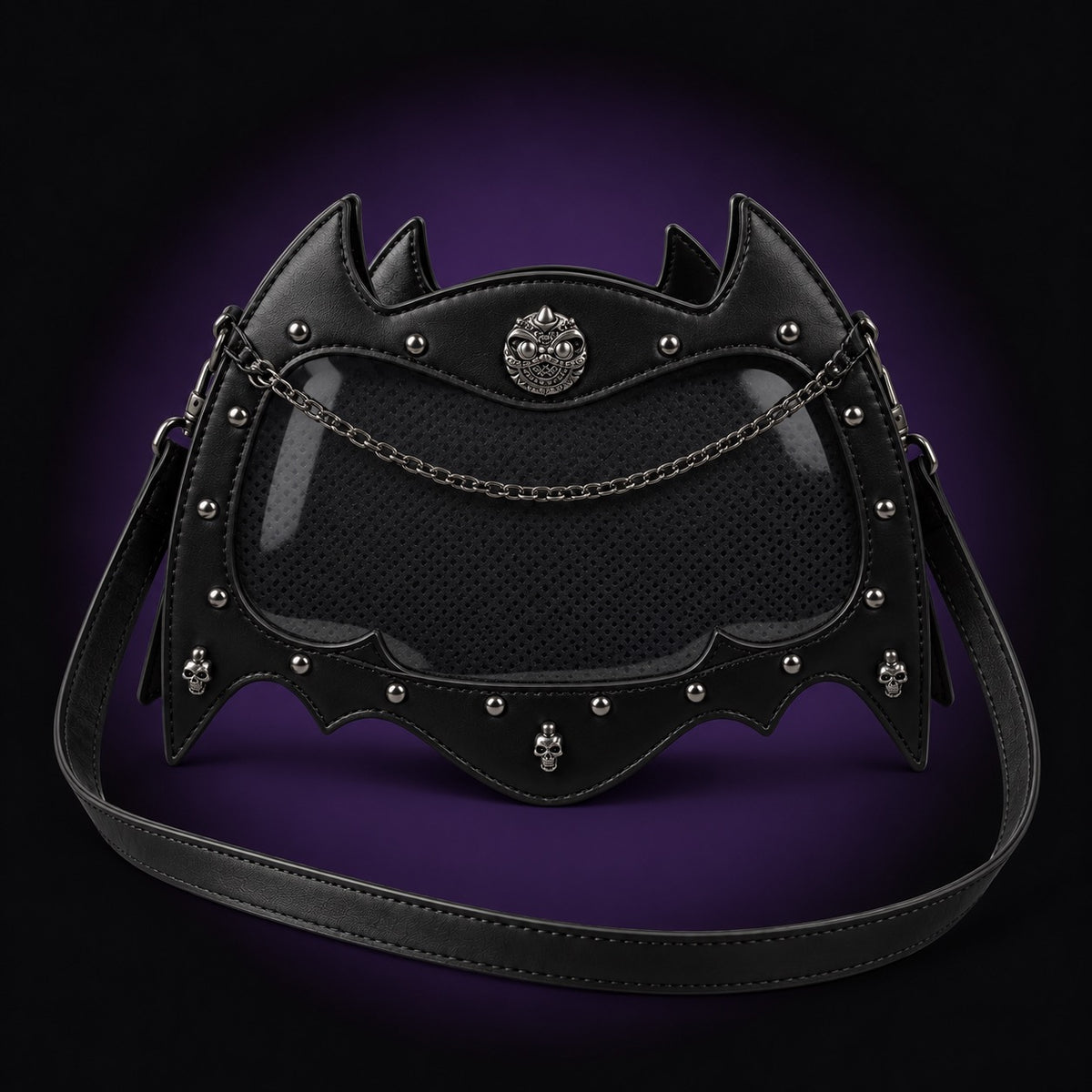Black bat-shaped ita bag with a clear display window over an empty black insert, silver-tone chain, skull rivets and a grinning cat emblem, on a dark violet background